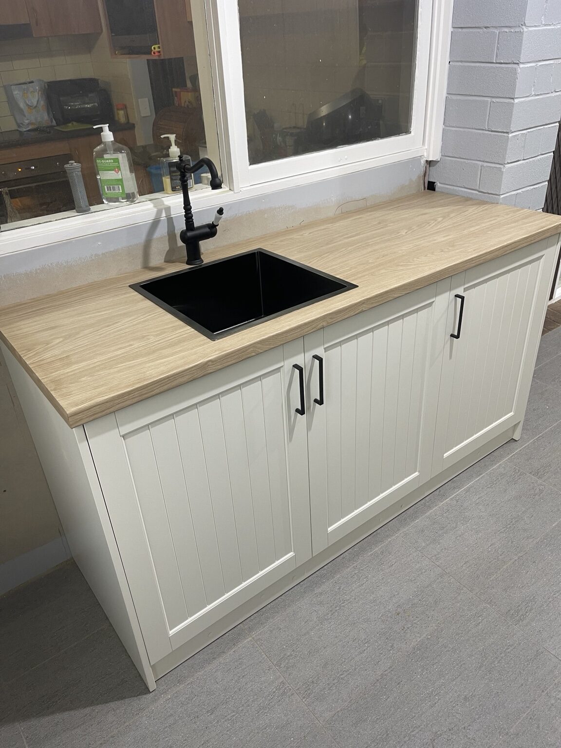 Completed laundry with custom white joinery, timber benchtop and black sink